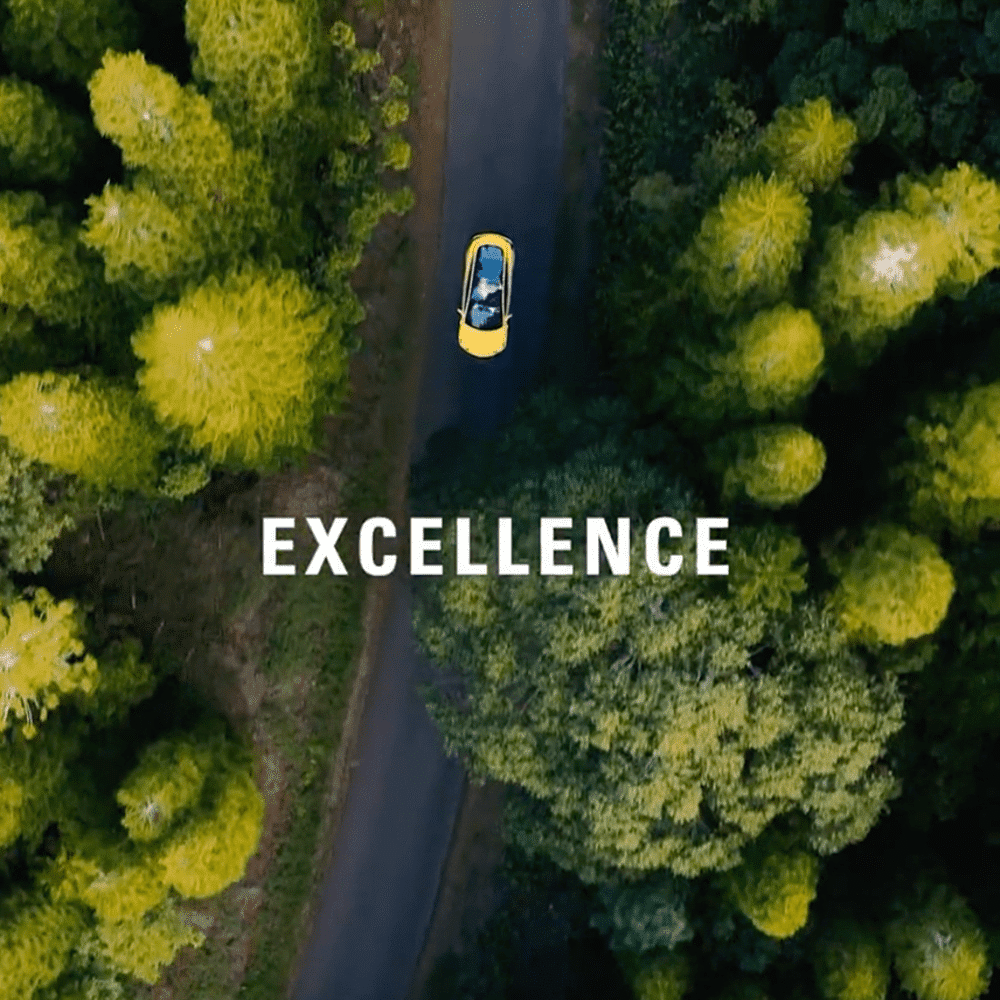 Car driving on tree-lined road from above with the word Excellence overlaid